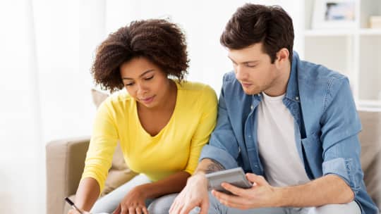 couple sitting on a couch writing a budget and holding a calculator