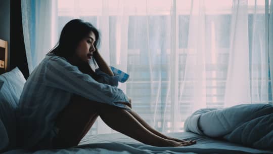 woman sitting on her bed looking depressed