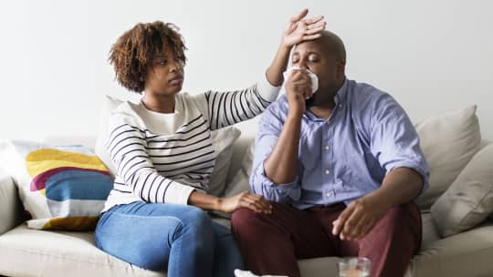 Couple sick at home on the sofa, woman checking partner's temperature