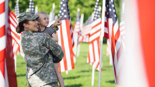 soldier holding daughter and pointing at flags