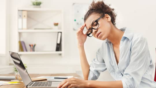 Frustrated woman looking away from laptop with hand to her forehead.