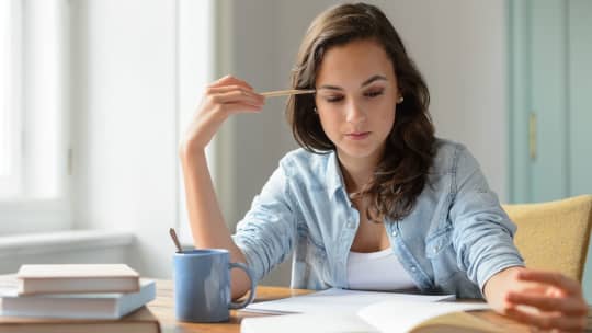 INTJ woman looking at a pile of papers with coffee and a pencil in hand