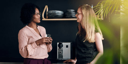 two women talking by a coffee machine
